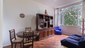 Zona pranzo con tavolo e sedie in legno, un mobile contenitore con ripiani e una finestra vista alberi.