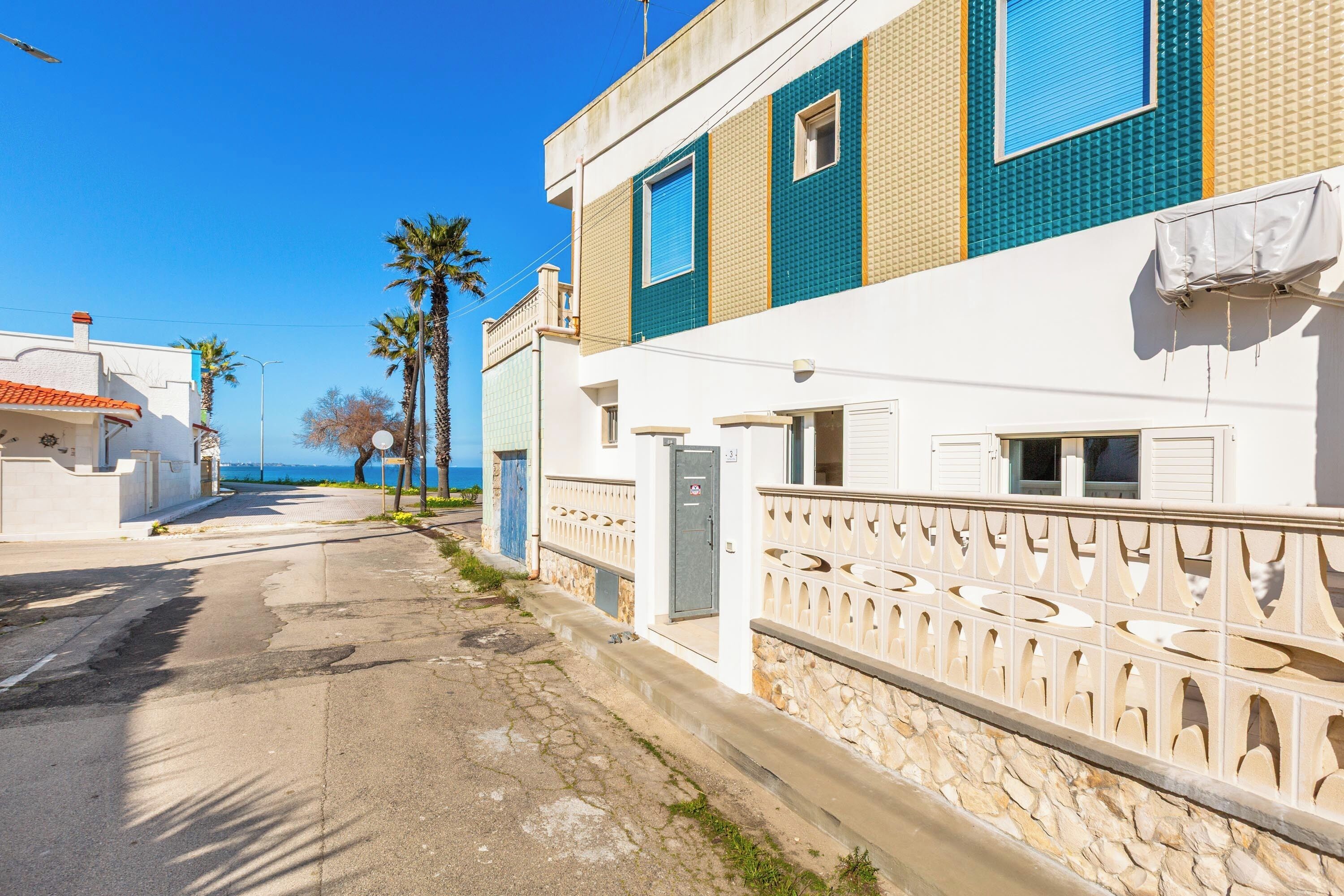 A coastal street with buildings, palm trees, and a clear sky.