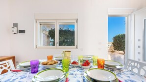 A dining table set with plates, glasses, and cutlery, a window with a view of trees, and a door leading outside. - Casa Blasi by BarbarHouse (San Pietro Vernotico)