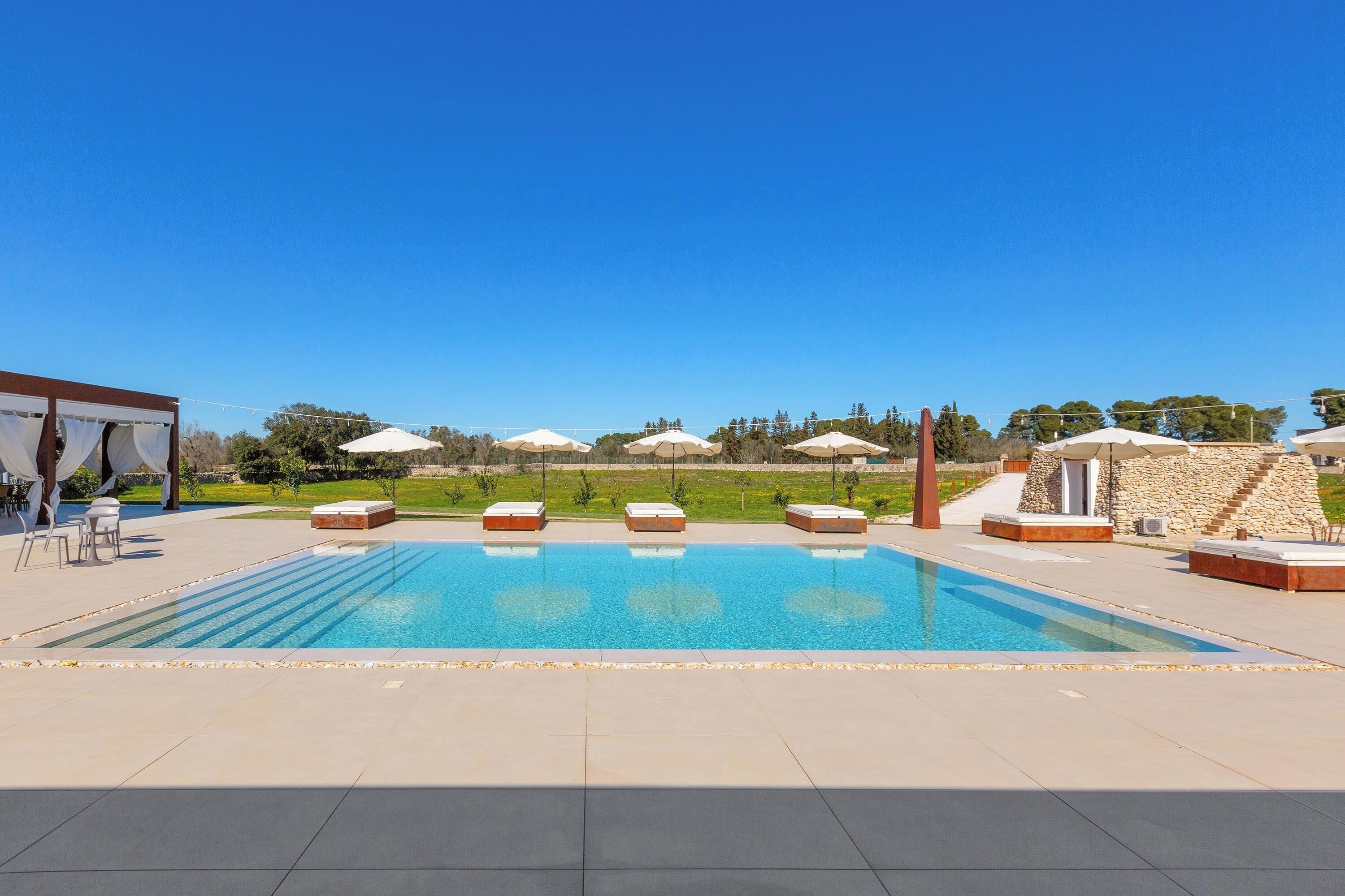 A swimming pool with lounge chairs, a covered seating area, and a view of the landscape.