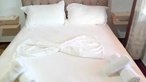 A neatly made bed with a towel arranged in a bow shape, a rolled towel, and a pillow.