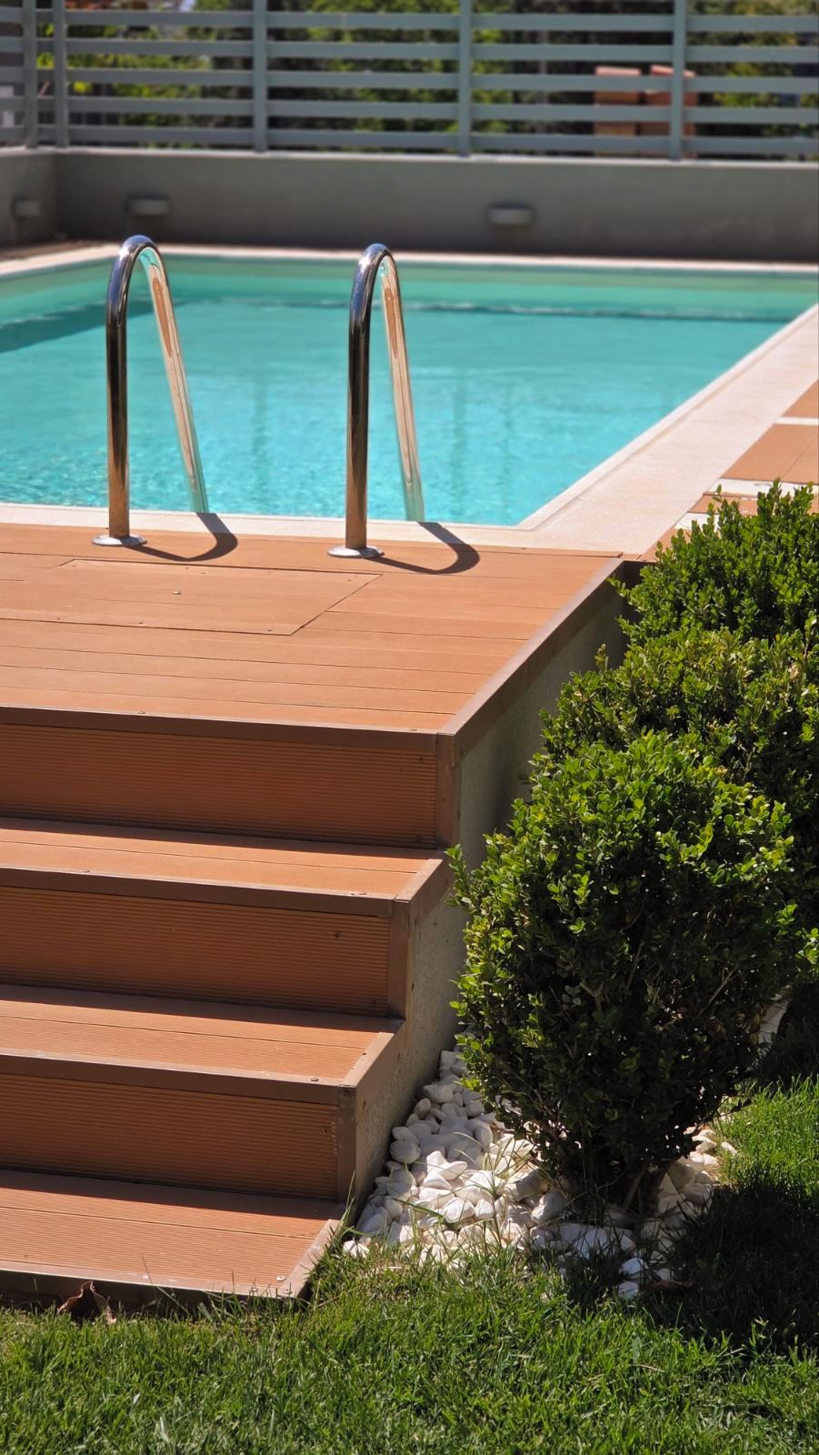 A swimming pool with steps leading into it, surrounded by greenery.