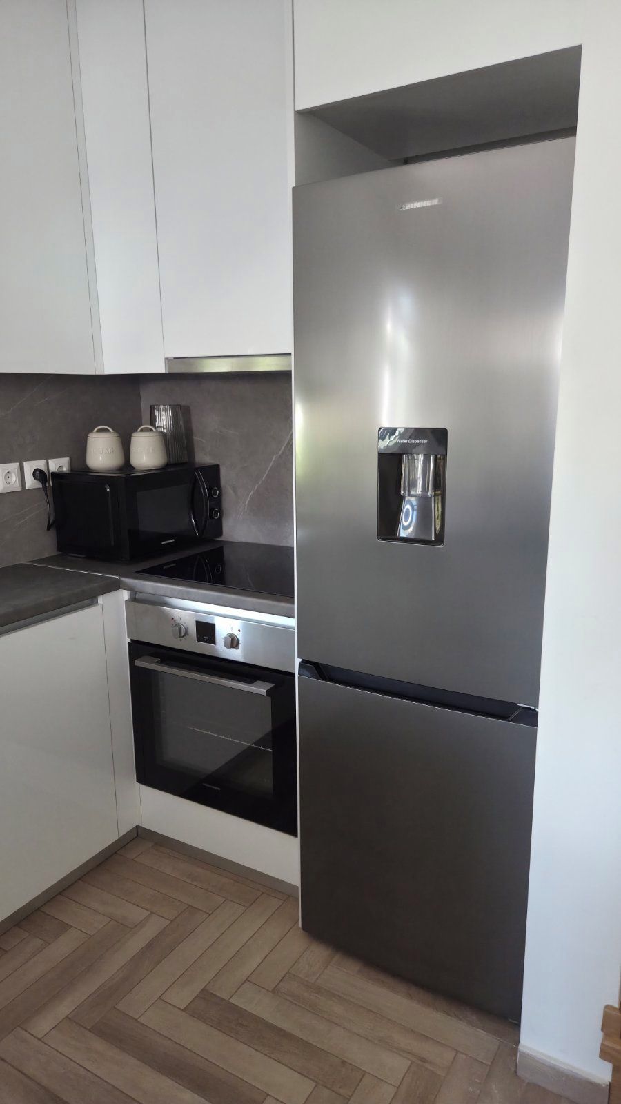 Una cocina con gabinetes blancos, un refrigerador de acero inoxidable, un horno empotrado y un microondas.