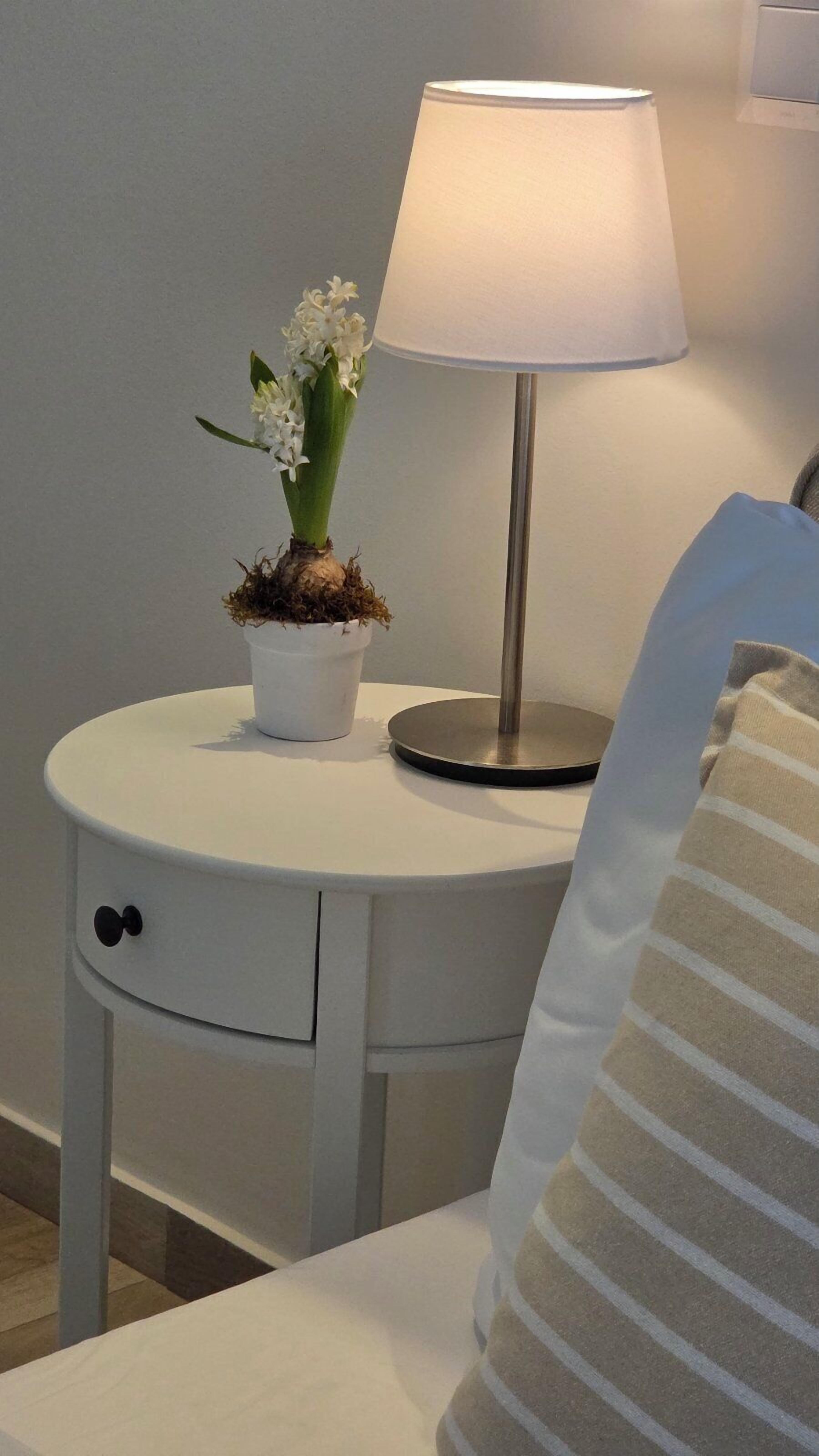 Une table de chevet avec une lampe, une plante en pot et un coussin à rayures.