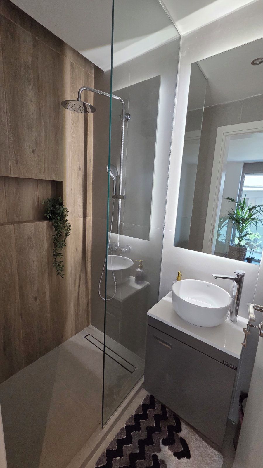A modern bathroom with a glass-enclosed shower, a white sink, and a mirror above the vanity.