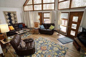 A spacious living room with leather sofas, a coffee table, and a large window with curtains. - Snow Chateau Adventure Lodge (Davis)