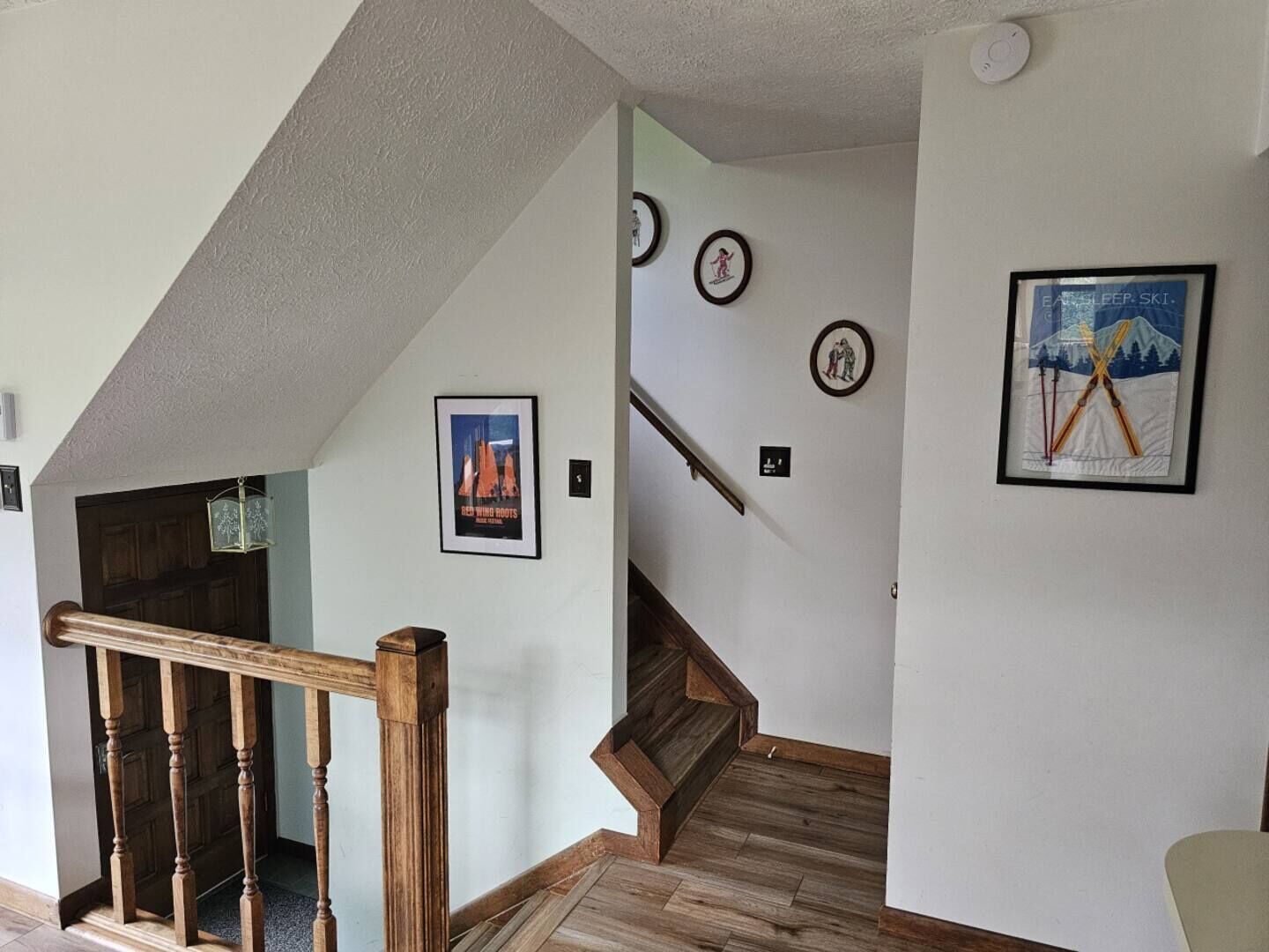 Un escalier avec des rampes en bois et un plancher en bois, menant à une pièce aux murs blancs et ornée de tableaux encadrés.
