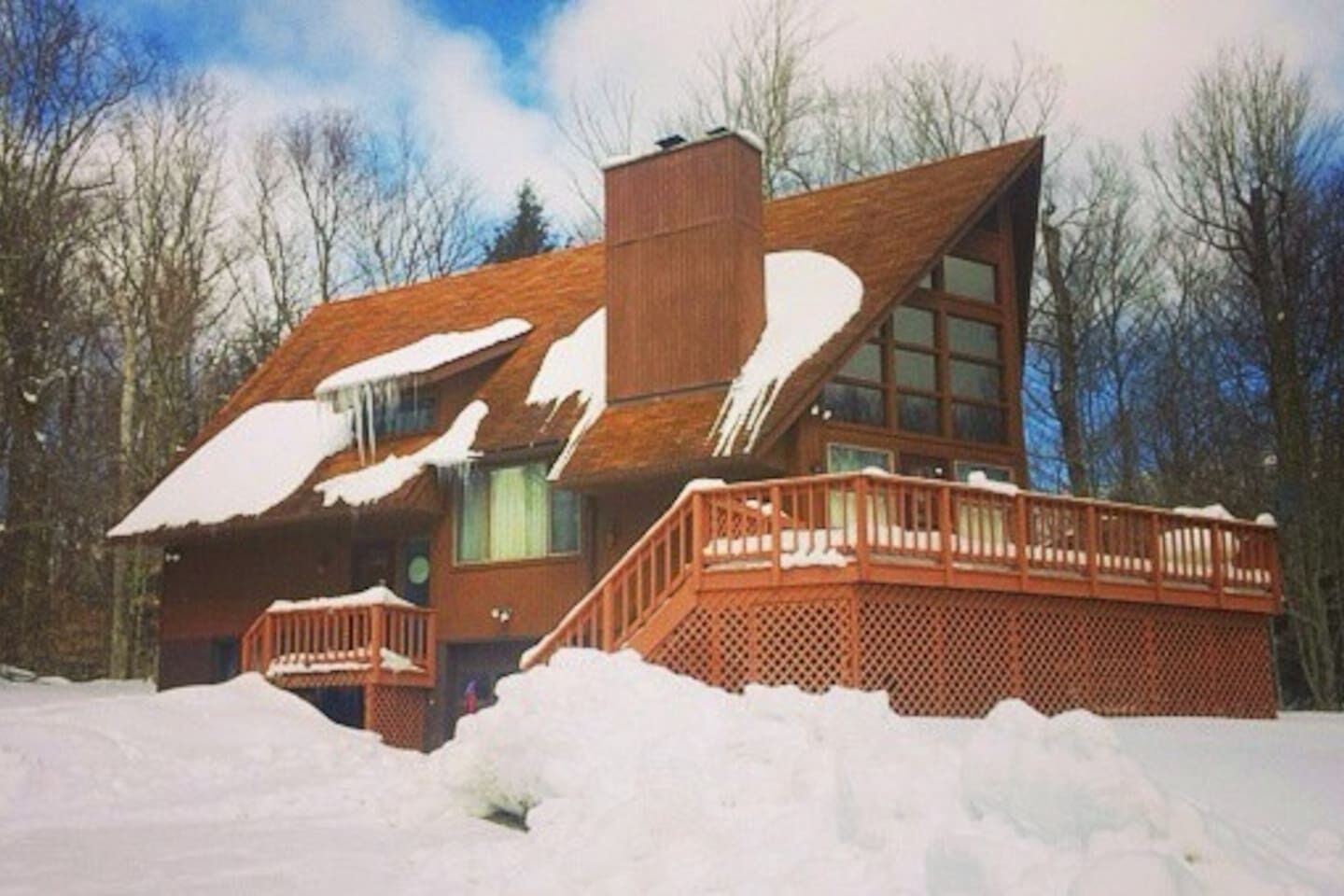 Une cabane en bois avec une grande cheminée, un balcon et un toit recouvert de neige.