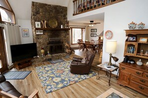 A spacious living room with a stone fireplace, a television, leather seating, and a dining area. - Snow Chateau Adventure Lodge (Davis)