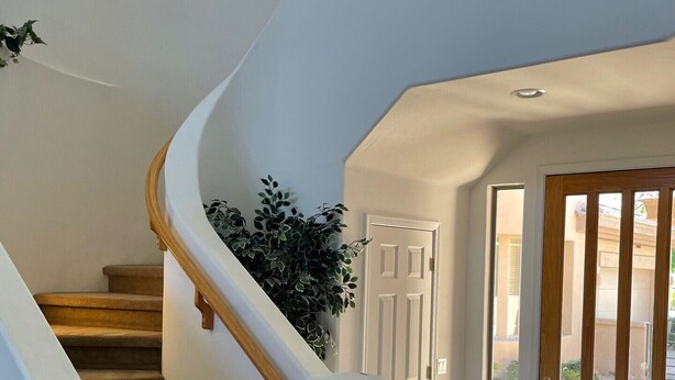 Un escalier en colimaçon, avec des marches recouvertes de moquette et des rampes en bois, menant à une porte dotée d’un panneau de verre.