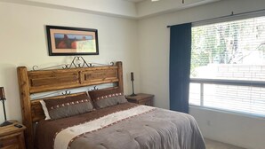 Une chambre à coucher avec une tête de lit en bois, une grande fenêtre offrant une belle vue, une table de chevet et un tableau encadré au mur.