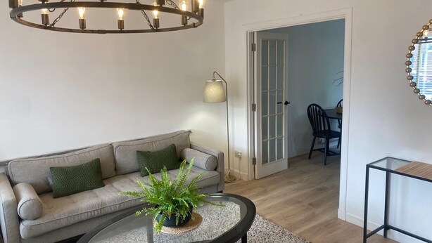 A living room with a sofa, a coffee table with a plant, a chandelier, and a lamp. - Modern 3 bed Home by Glasgow Airport (Paisley)