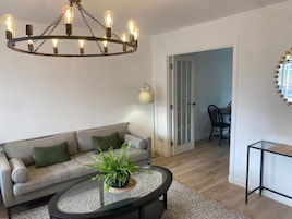 Una sala de estar con un sofá, una mesa de centro con una planta, una araña y una lámpara.