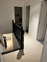 Una escalera con alfombra y barandilla, que conduce a una habitación con cama y mesita de noche.