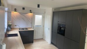 A modern kitchen with a marble backsplash, a built-in stove, and dark cabinetry. - Modern 3 bed Home by Glasgow Airport (Paisley)