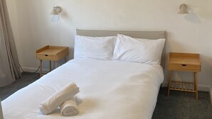 A neatly made bed with white linens, two bedside tables, and wall-mounted lamps. - Modern 3 bed Home by Glasgow Airport (Paisley)