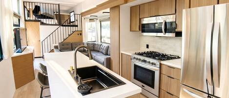 A modern kitchen with a central island, stainless steel appliances, and a staircase leading to a living area.