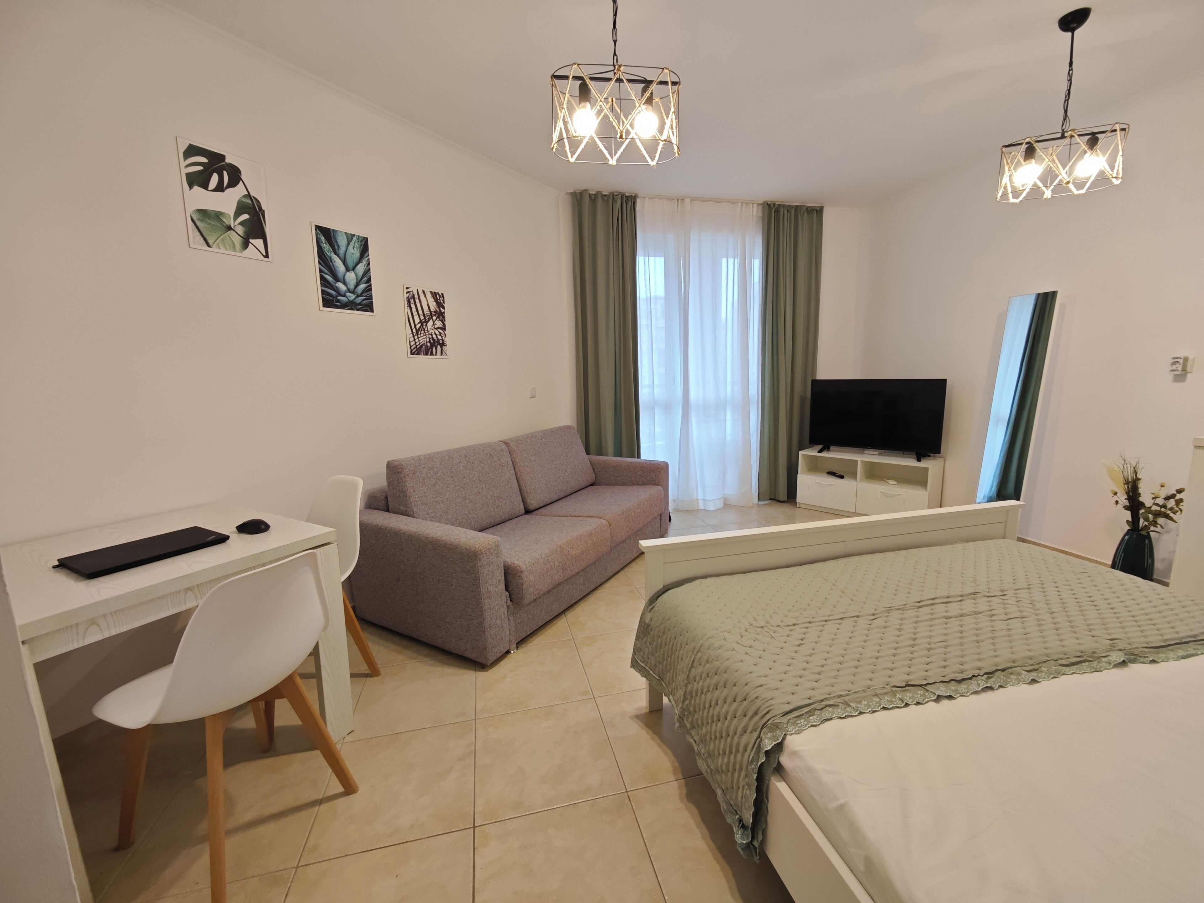 Habitación de hotel con cama, escritorio con computadora, sofá, televisión y obras de arte en las paredes.