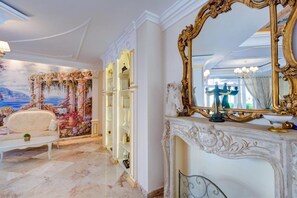 Ein luxuriöses Zimmer mit einer weißen Couch, einem dekorativen Wandgemälde, einem großen, verzierten Spiegel und einem Marmorboden.