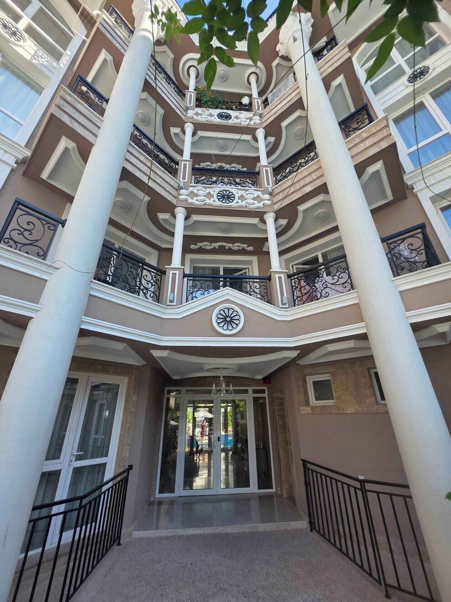 Ein mehrstöckiges Gebäude mit einem zentralen Atrium, Balkonen mit aufwendigen Geländern und einer großen Ziffernblattuhr.