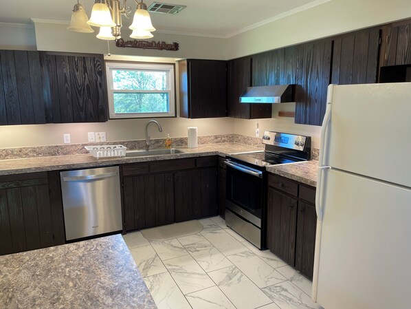 A kitchen with dark wood cabinets, a stainless steel dishwasher, a double oven, and a refrigerator.