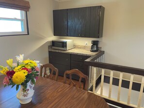 A kitchen with a microwave, coffee maker, and dark cabinets. There is a dining table with chairs and a vase of flowers. - Charming 4BR home with many extras in a quiet neighborhood 30 min from downtown. (Saint Rose)