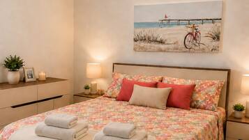 Ein Schlafzimmer mit einem Bett, zwei Nachttischen, einem Wandbild und einer Zimmerpflanze.