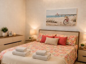 Un dormitorio con cama, dos mesitas de noche, una mesita auxiliar, un cuadro en la pared y una planta en maceta.