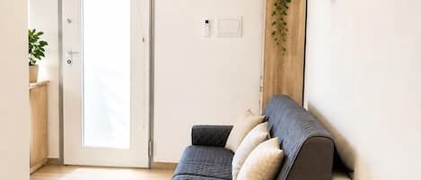 A modern living room with a sofa, a door, a wall-mounted plant, and a light switch.