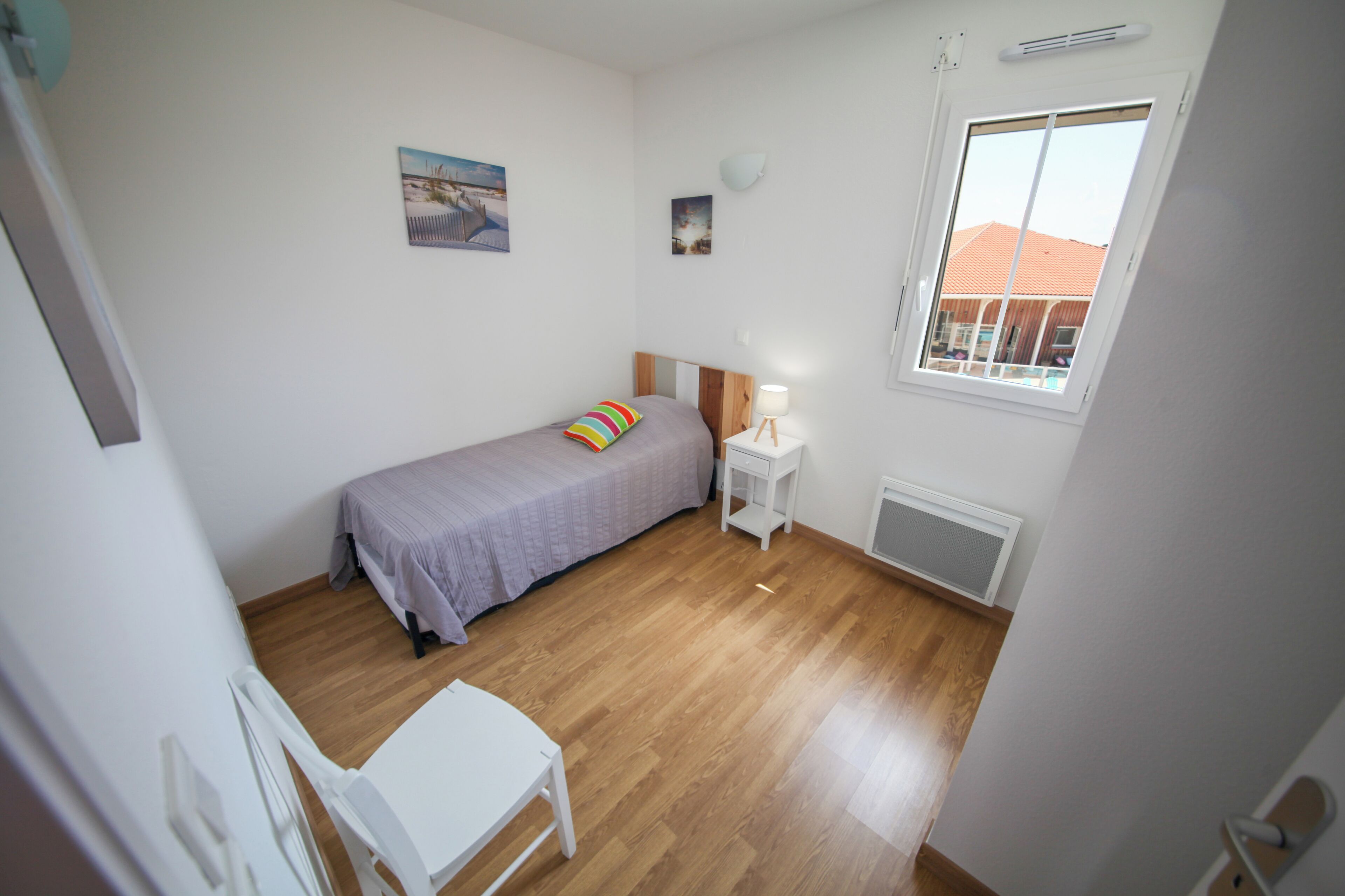 Een slaapkamer met een bed, een stoel, een tafeltje, een raam en een radiator.