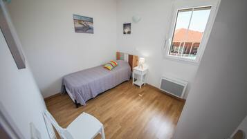 Een slaapkamer met een bed, een stoel, een tafeltje, een raam en een radiator.
