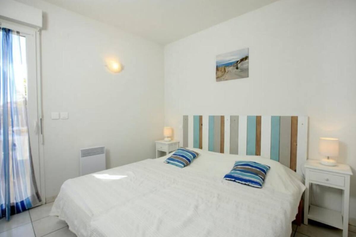A bedroom with a bed, two bedside tables, a nightstand, a window with curtains, and a wall-mounted picture.