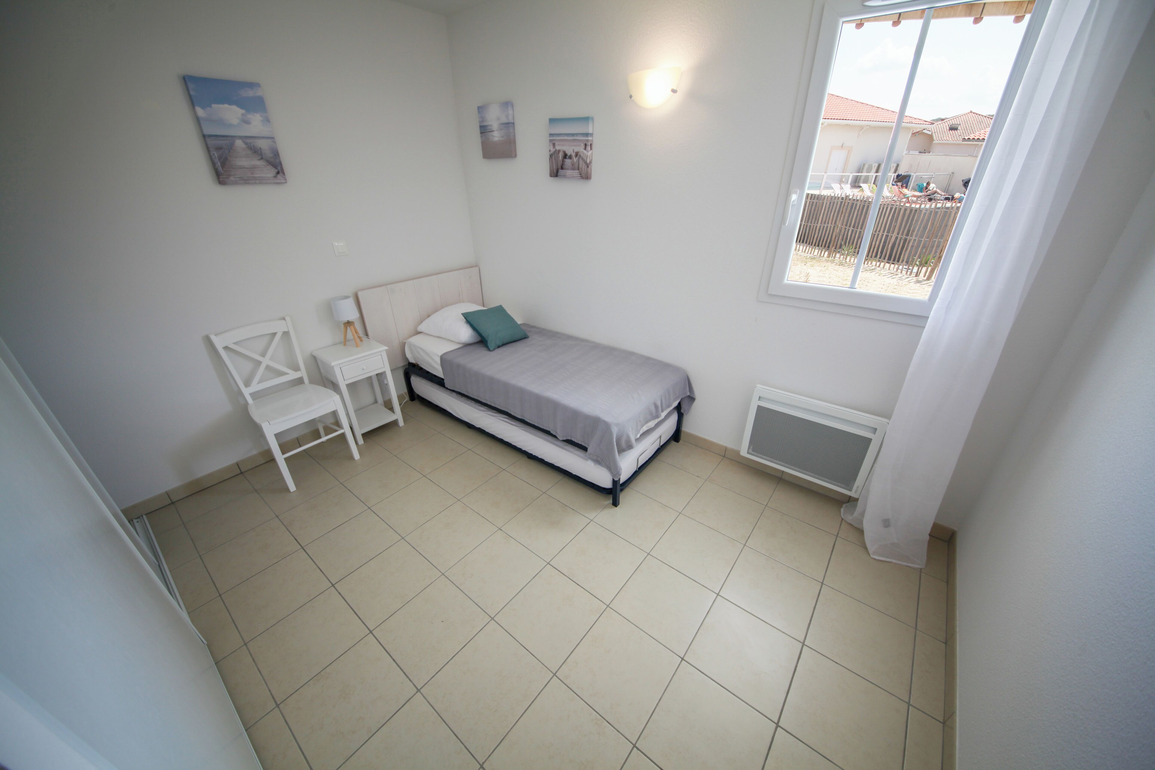 Una habitación pequeña y limpia con una cama individual, una mesita de noche, una silla y una ventana con vistas al exterior.