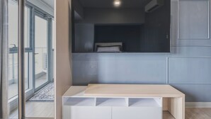 Ein modernes Zimmer mit großem Fenster, einem flachbildfernseher an der Wand und einem Holztisch.