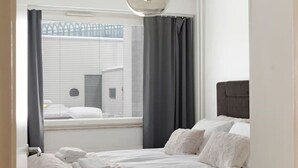 A bedroom with a bed, a hanging light fixture, a window with curtains, and a view of buildings outside. - Funky City Apartment By Lapland Host (Rovaniemi)
