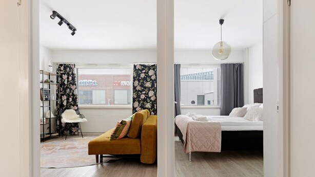 A room with a bed, a sofa, a chair, a lamp, and a window with curtains. - Funky City Apartment By Lapland Host (Rovaniemi)
