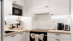 A modern kitchen with white cabinets, a microwave, a coffee maker, a toaster, and a hanging oven mitt. - Funky City Apartment By Lapland Host (Rovaniemi)