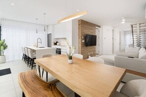 A modern kitchen with a dining area, a living room with a sofa, and a TV mounted on the wall. - Luxury 2BR Condo w/ Rooftop Jacuzzi & Water Views (Laval)