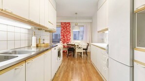 Eine moderne Küche mit weißen Schränken, einer Holztischplatte, einem Esstisch mit Stühlen und einem roten Blumenvorhang.