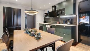 A modern kitchen with a dining area, featuring a wooden table, chairs, a hanging light fixture, and built-in appliances.