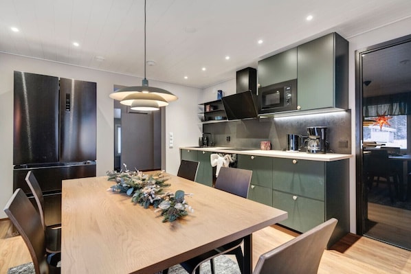 Una cocina moderna con comedor, que incluye una mesa de madera, sillas, una lámpara colgante y electrodomésticos integrados.