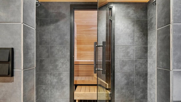 A modern shower area with a glass door, a wooden bench, and a black towel rack.