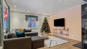 A modern living room with a sectional sofa, a Christmas tree, a flat-screen TV, and a decorative stove.