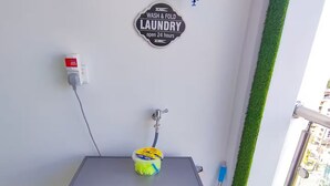 Eine kompakte Waschmaschine mit Bedienfeld, einer Steckdose und einem Schild an der Wand mit der Aufschrift 'WASH & FOLD LAUNDRY'.