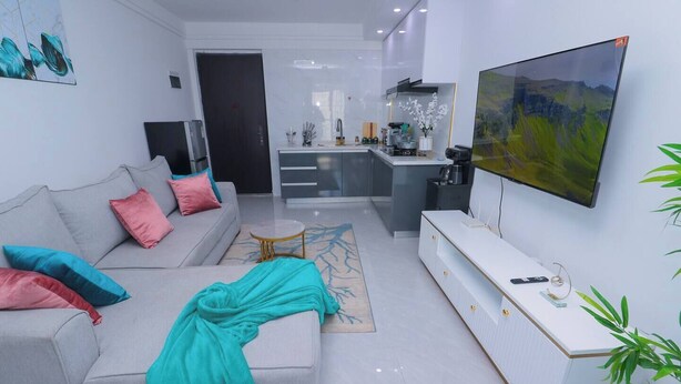 Ein modernes Wohnzimmer mit einer Couch, einem Couchtisch, einem Fernseher und einer Küchenzeile im Hintergrund.