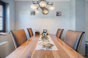 Un espace repas comprenant une table en bois, des chaises en cuir, un lustre et des œuvres d’art murales.