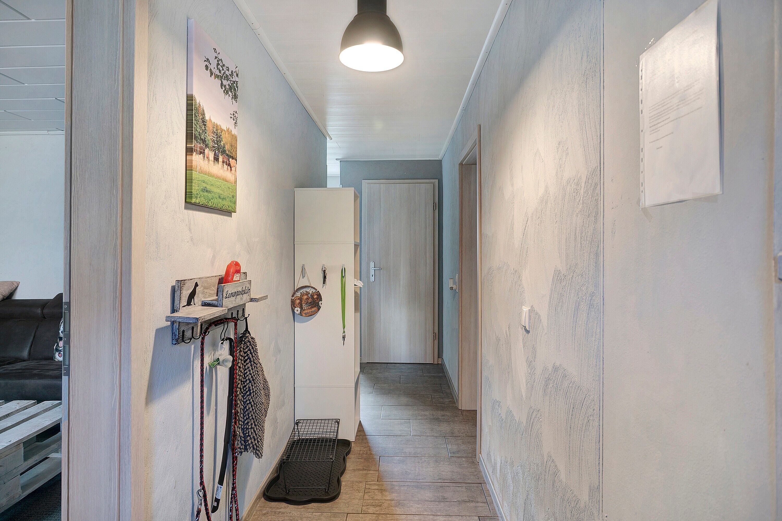 A narrow hallway with a wooden floor, a coat rack, a pet gate, and a door at the end.