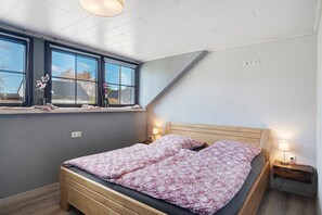 Une chambre à coucher avec un lit, une fenêtre donnant sur un beau paysage, une table de chevet avec une lampe et une prise électrique au mur.