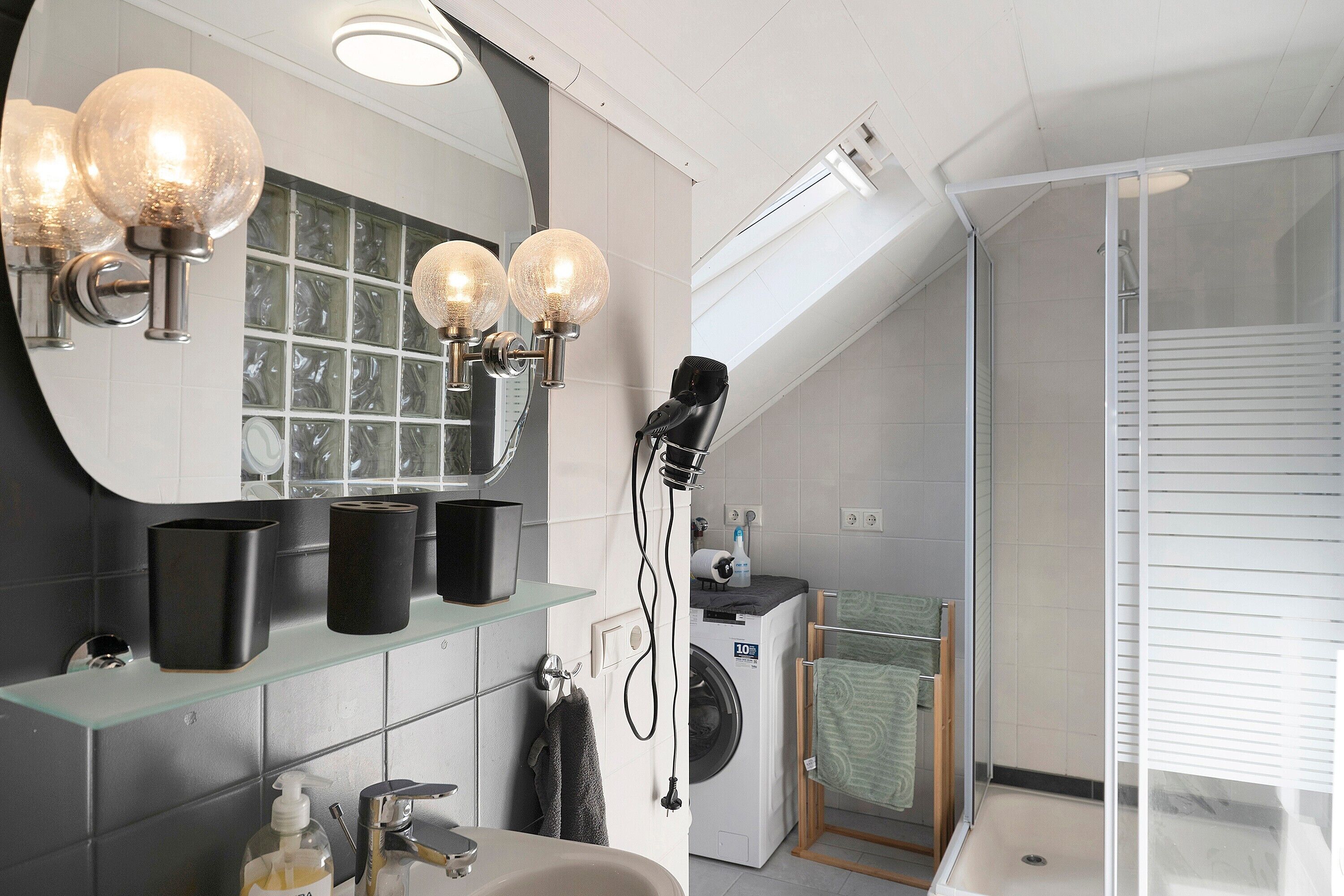 A modern bathroom with a glass shower enclosure, a hairdryer, and a washing machine.