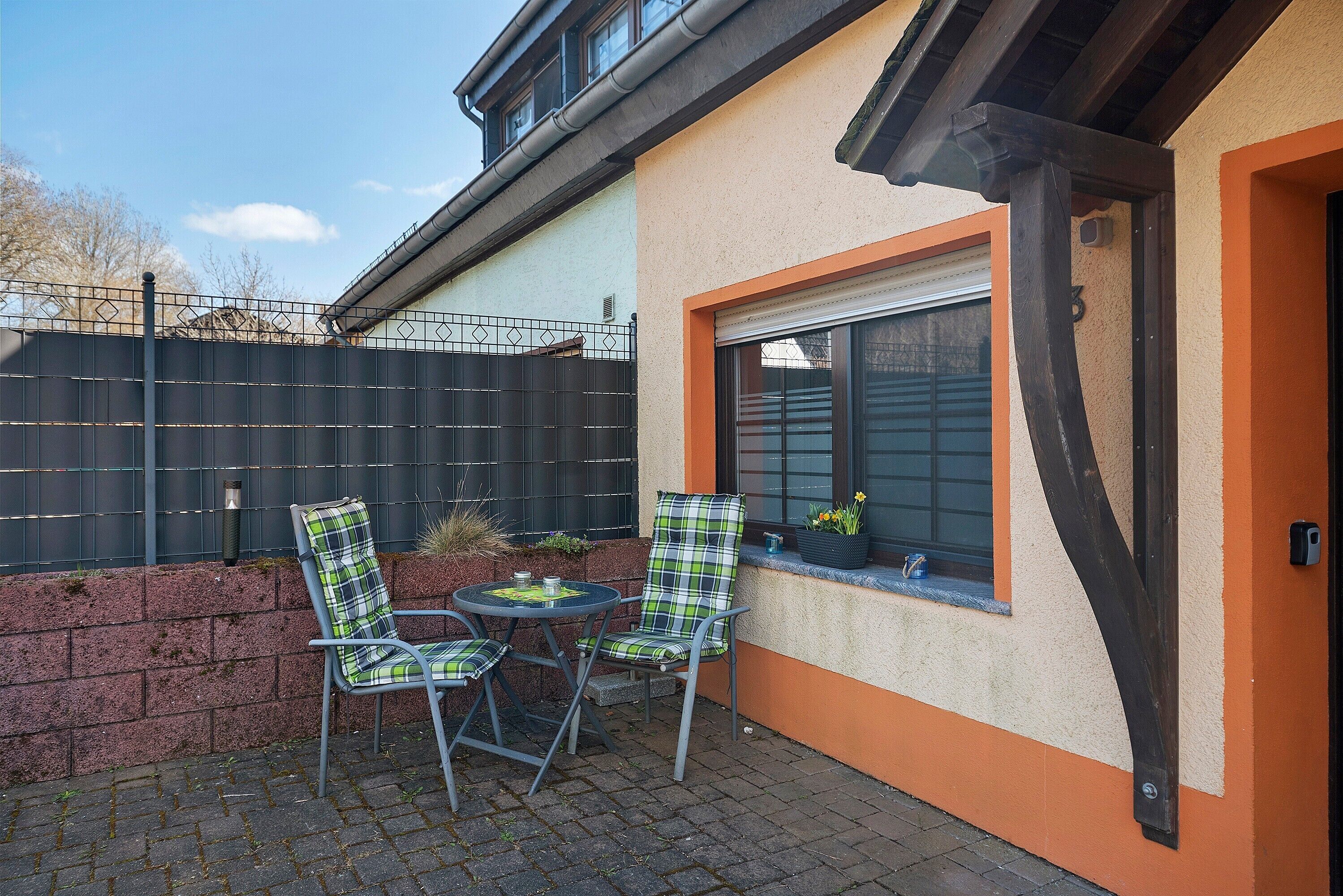An outdoor seating area with two chairs and a table, a window with a view, and a door to the right.
